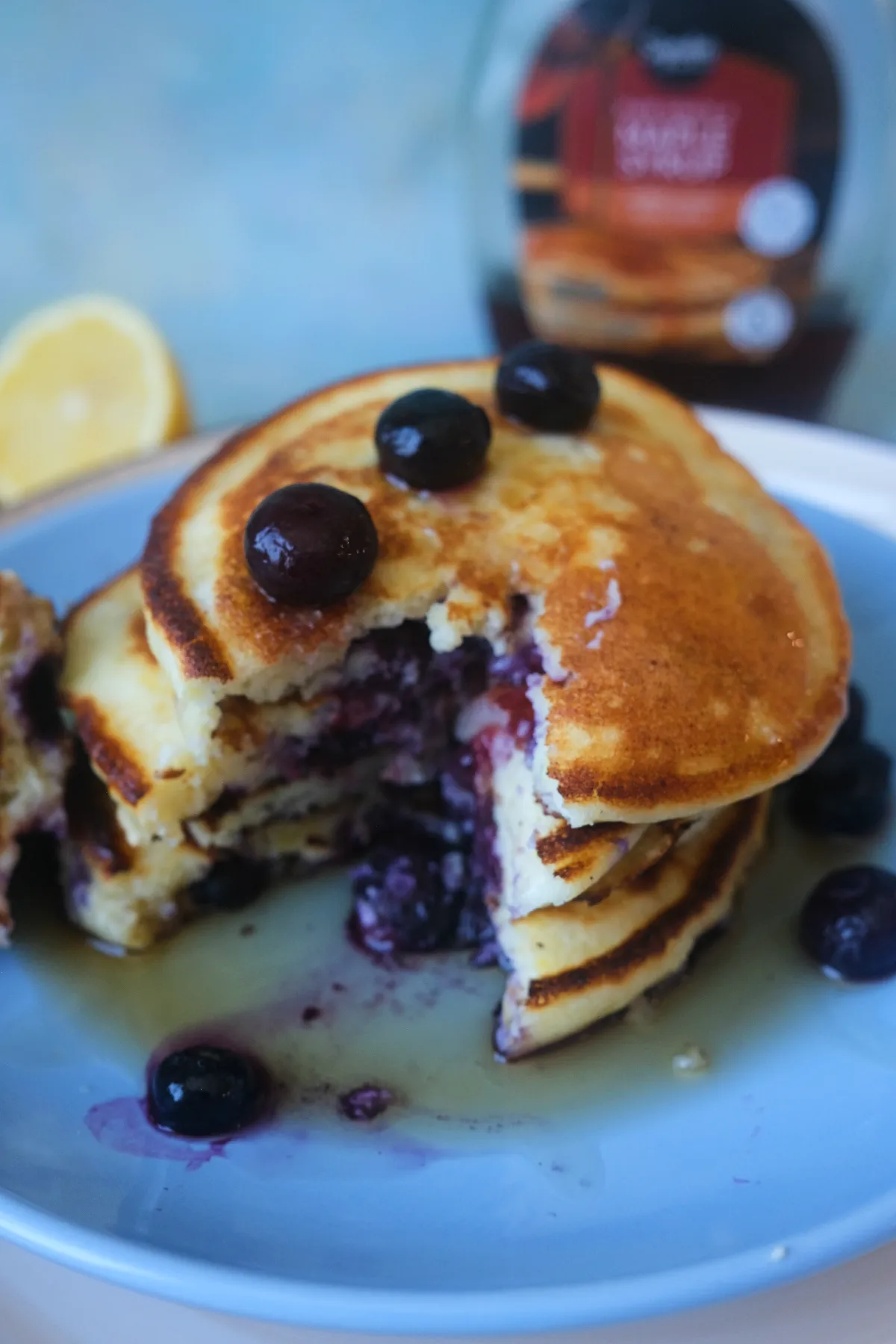 Cut lemon blueberry ricotta pancakes drizzled with maple syrup and topped with fresh blueberries on a white plate.