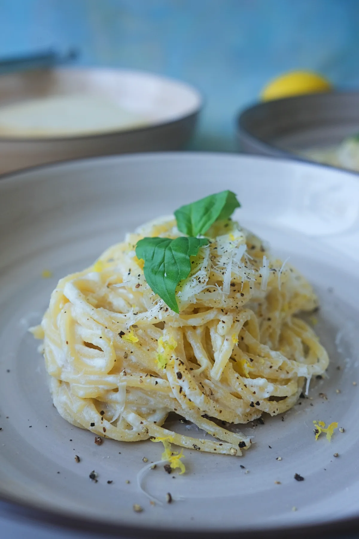 A serving of lemon ricotta pasta topped with grated Parmesan, fresh basil leaves, cracked black pepper, and lemon zest on a gray ceramic plate.