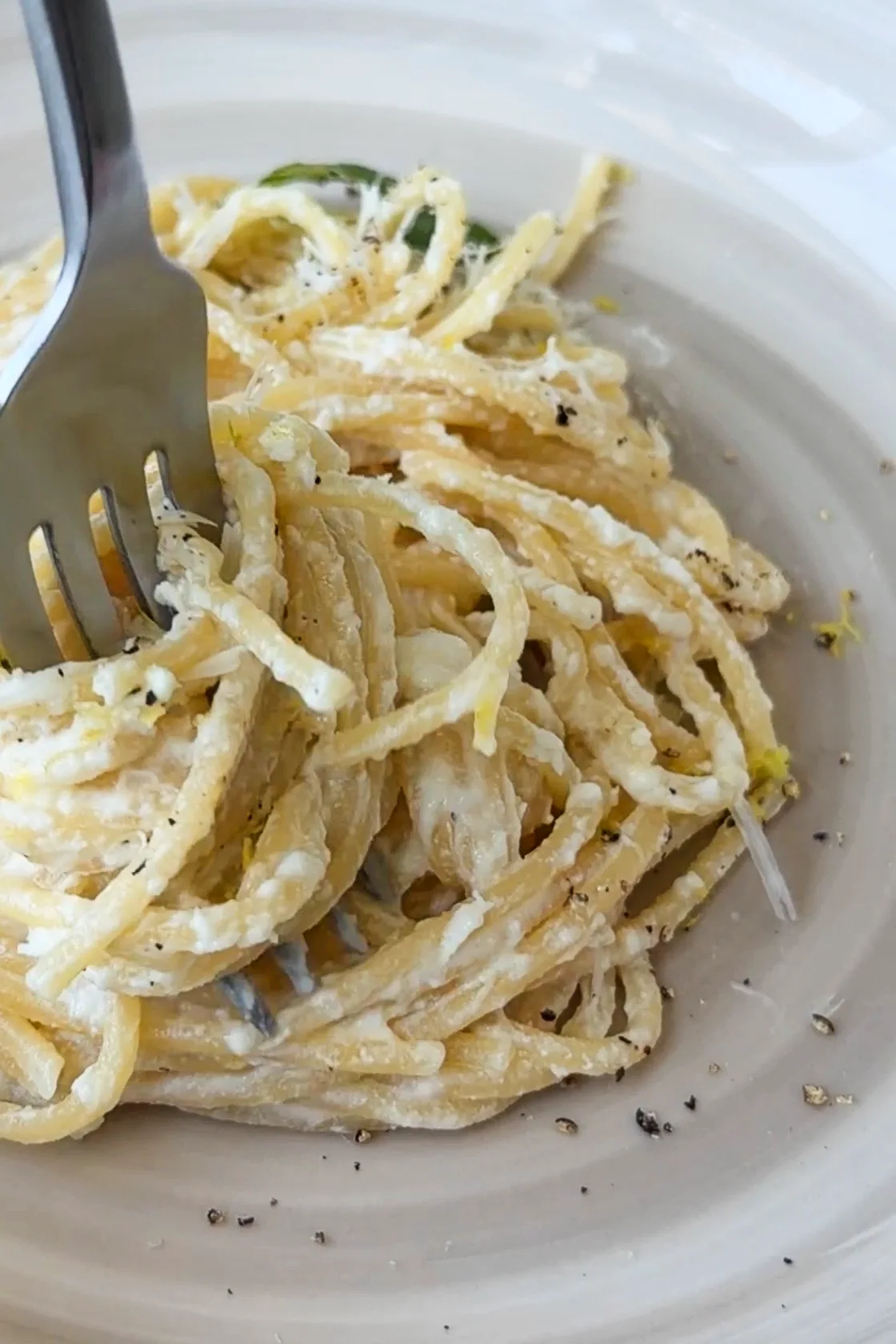 A close-up of creamy lemon ricotta spaghetti coated in ricotta sauce with cracked black pepper and lemon zest as a fork twirls the pasta.