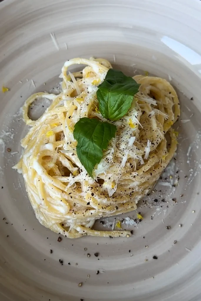 Creamy lemon ricotta spaghetti topped with grated Parmesan, cracked black pepper, and lemon zest on a gray ceramic plate.