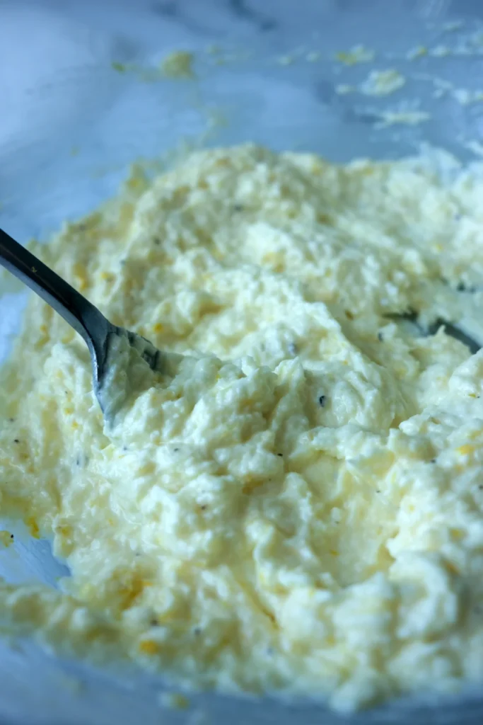 A close-up of lemon ricotta sauce mixed with grated Parmesan, lemon zest, and black pepper in a glass bowl.