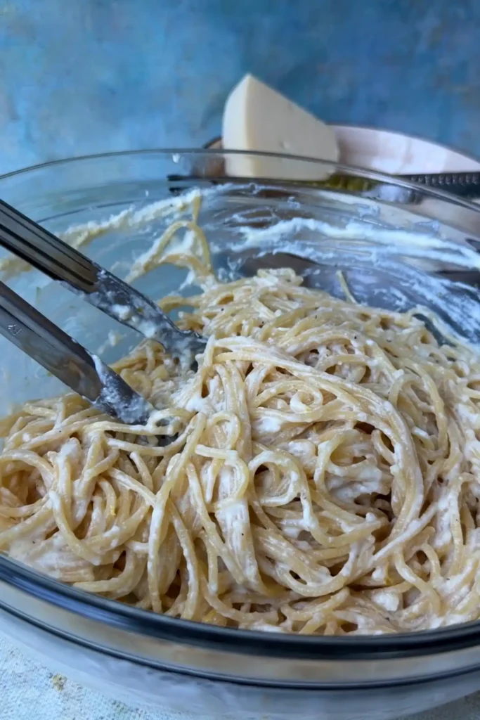 Creamy lemon ricotta spaghetti tossed in a glass bowl until the sauce evenly coats each strand of pasta.