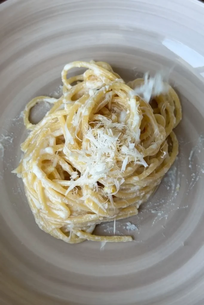 Freshly grated Parmesan cheese being sprinkled over creamy lemon ricotta spaghetti before serving.