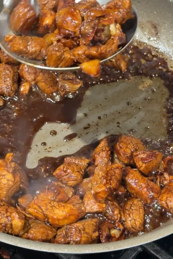 Cooked pork loin cubes coated in a glossy garlic butter soy sauce in a skillet.