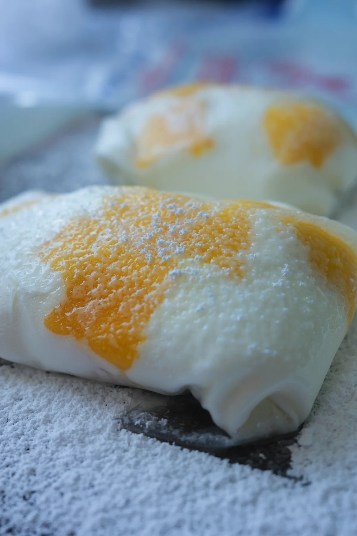 Close-up of a rice paper mango mochi coated in a potato starch and powdered sugar mixture on a dark serving board.