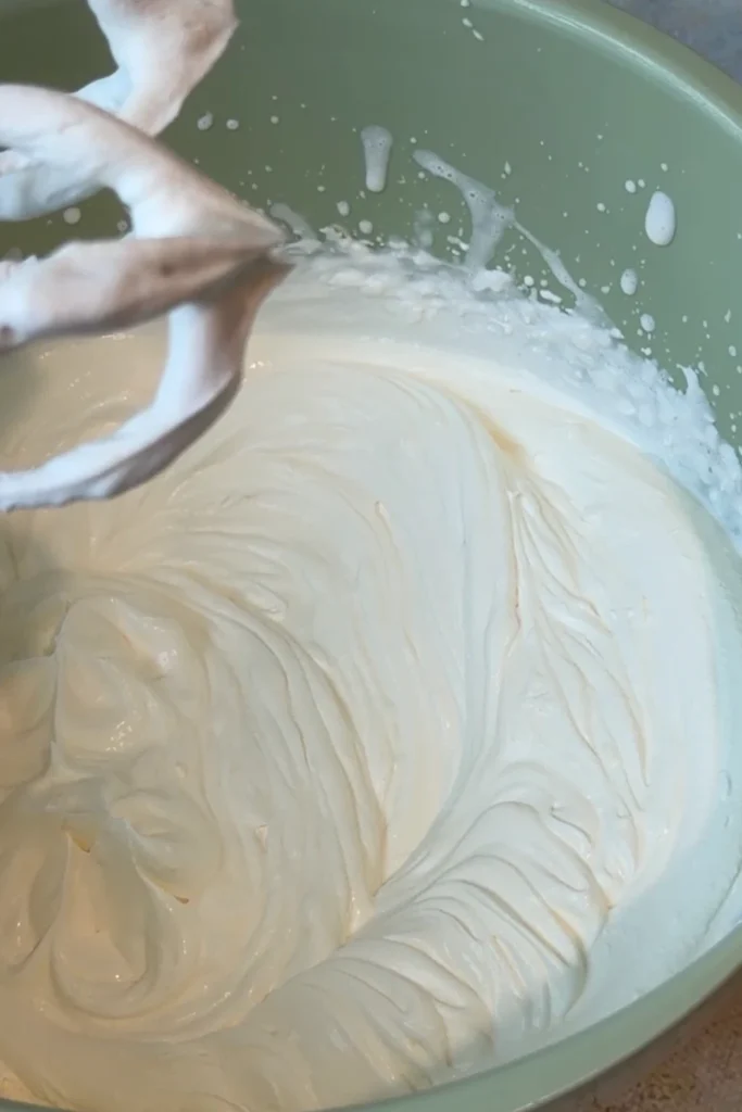 Whipped heavy cream and mango Greek yogurt mixed together until smooth and fluffy in a large mixing bowl.