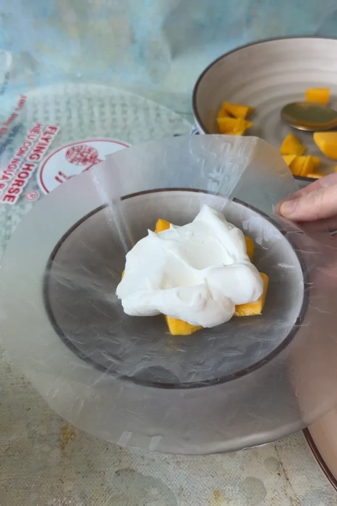 A scoop of whipped mango cream added on top of fresh mango pieces in the center of a softened rice paper wrapper.