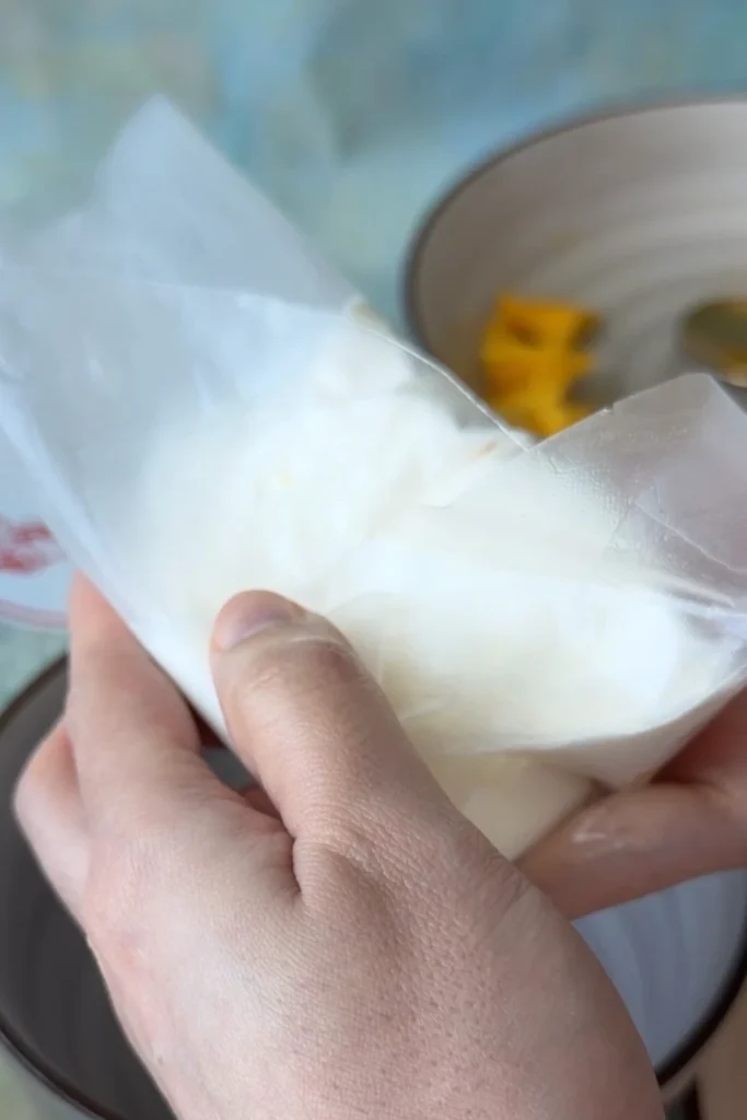 Hands folding a softened rice paper wrapper around the mango and whipped cream filling to form a sealed parcel.