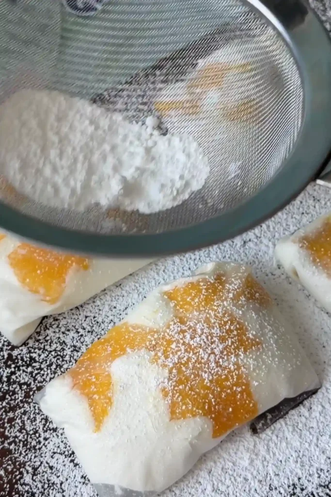 Potato starch and powdered sugar being sifted over homemade rice paper mango mochi arranged on a serving board.