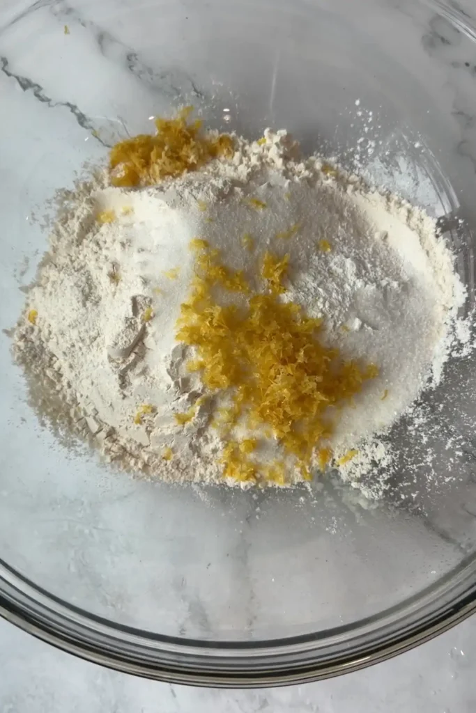 Flour, sugar, baking powder, salt, and lemon zest in a glass mixing bowl.
