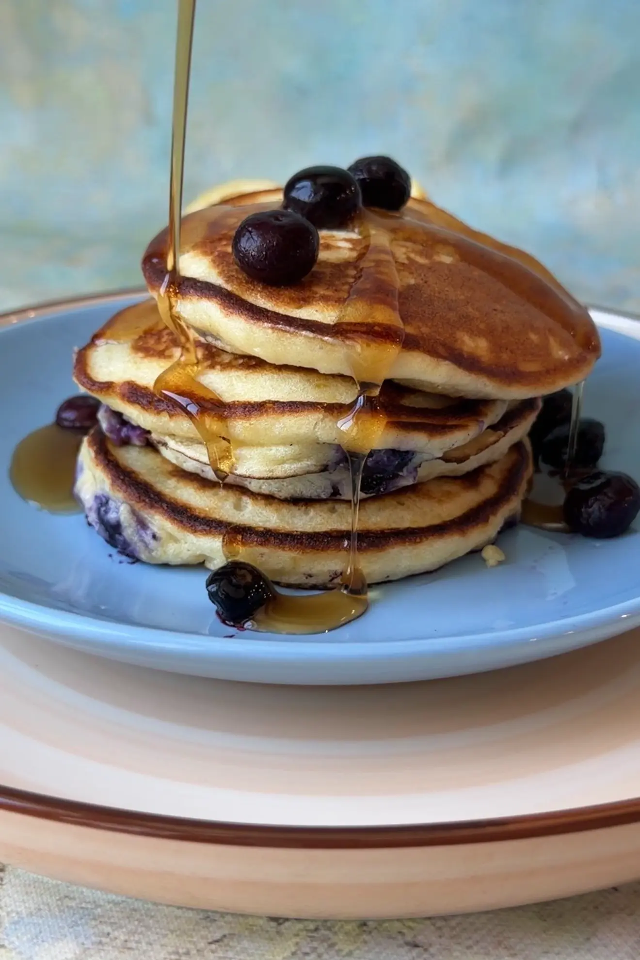 Stack of lemon blueberry ricotta pancakes topped with fresh blueberries and maple syrup on a white plate.