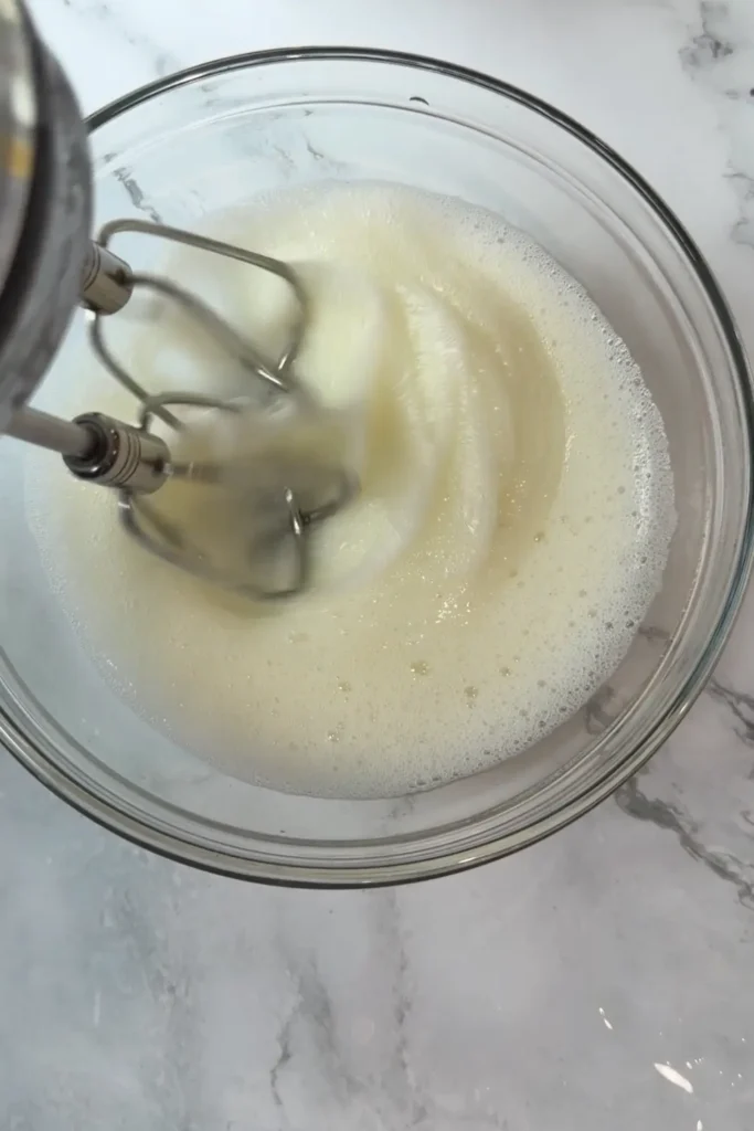 Egg whites being whipped with a hand mixer until foamy.