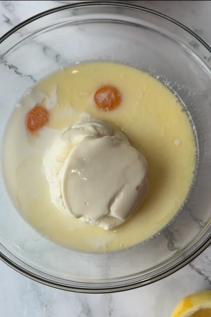Ricotta cheese, egg yolks, milk, and melted butter in a glass mixing bowl.