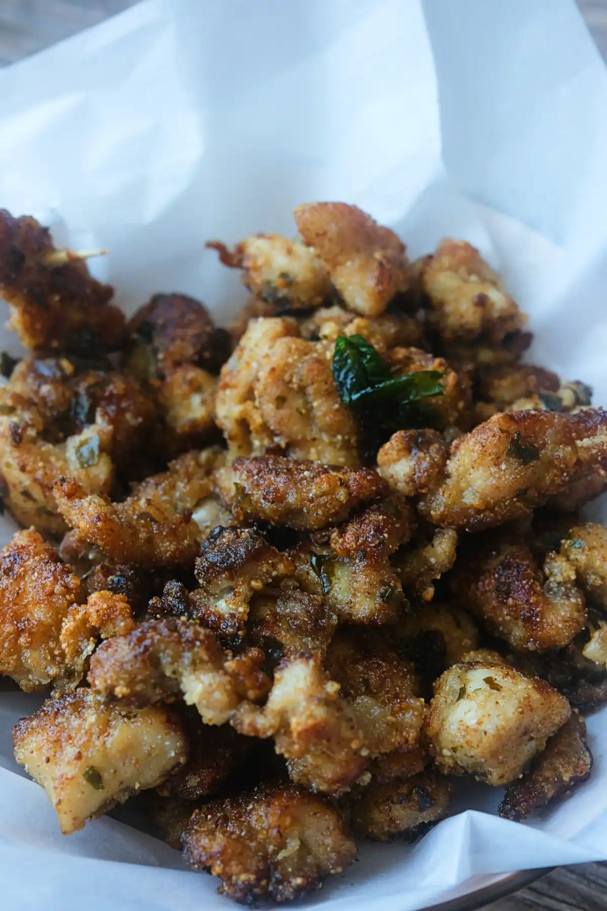 Taiwanese popcorn chicken piled on parchment paper with crispy fried basil and five-spice seasoning