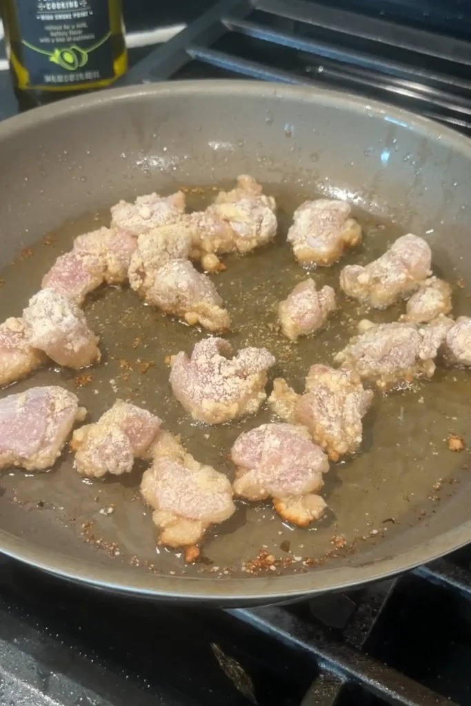 Sweet potato starch-coated chicken frying in hot oil in a skillet.
