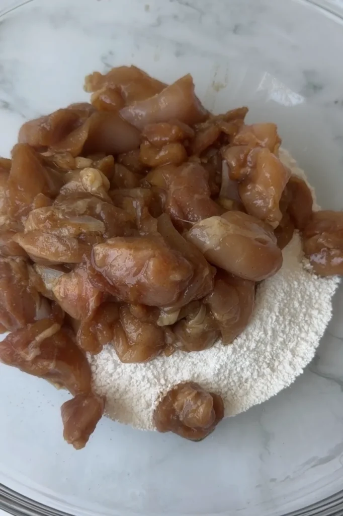 Marinated chicken added to a bowl of sweet potato starch before coating.