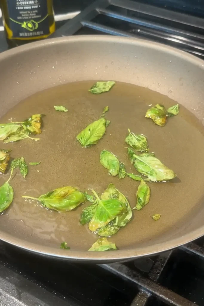 Fresh basil leaves frying in hot oil in a skillet.