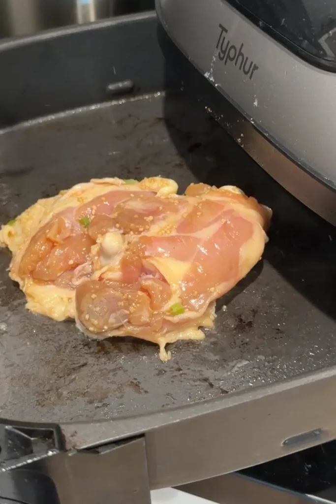 Marinated bone-in chicken thigh placed skin-side down in the air fryer basket before cooking until juicy inside with crispy caramelized skin.