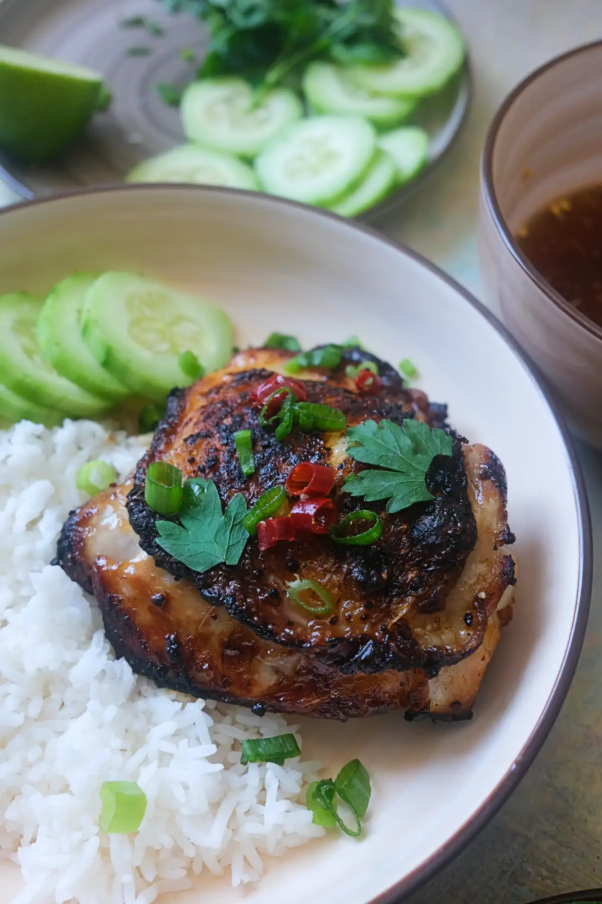 Close-up bowl of air fryer Vietnamese lemongrass chicken with crispy skin, fresh cucumber slices, steamed white rice, herbs, and nước chấm dipping sauce on the side.