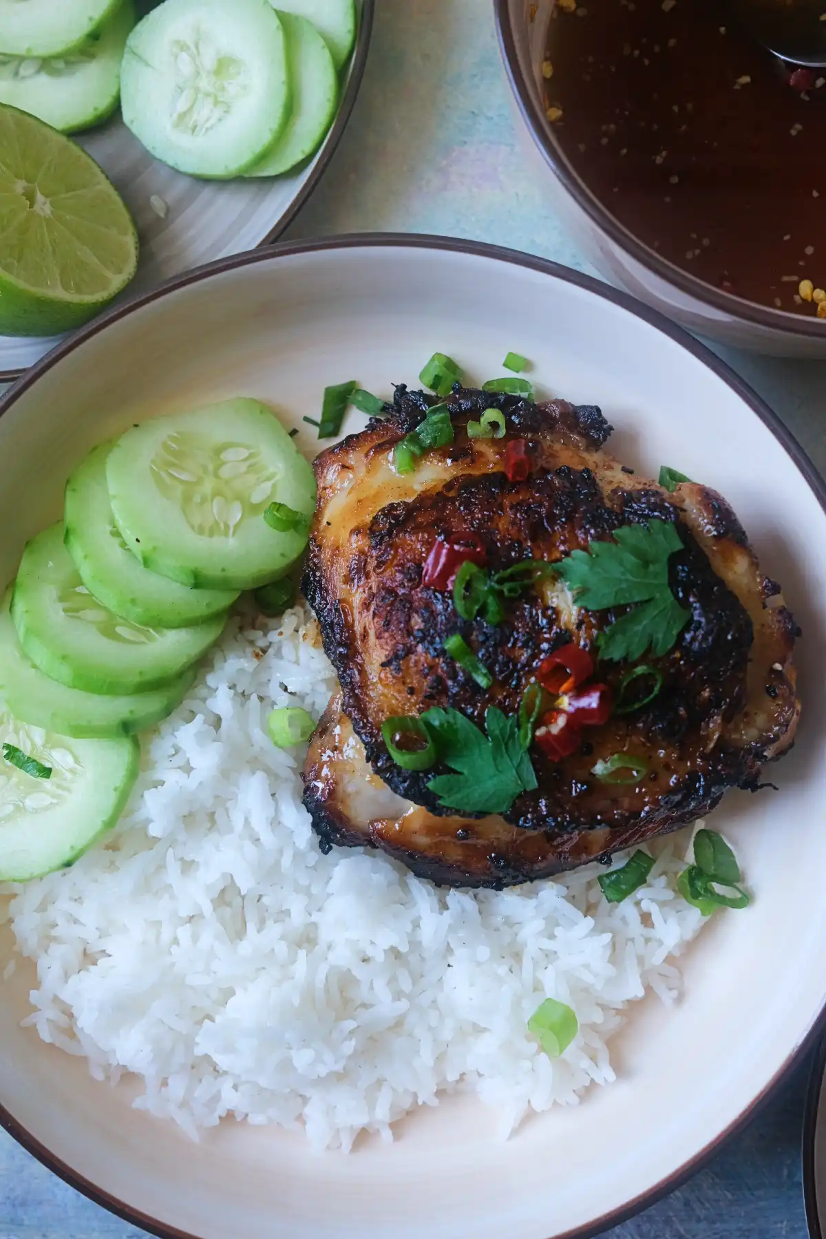 Overhead shot of Vietnamese lemongrass chicken with jasmine rice, cucumber slices, lime, scallions, cilantro, and nước chấm sauce for a flavorful Vietnamese-inspired meal.