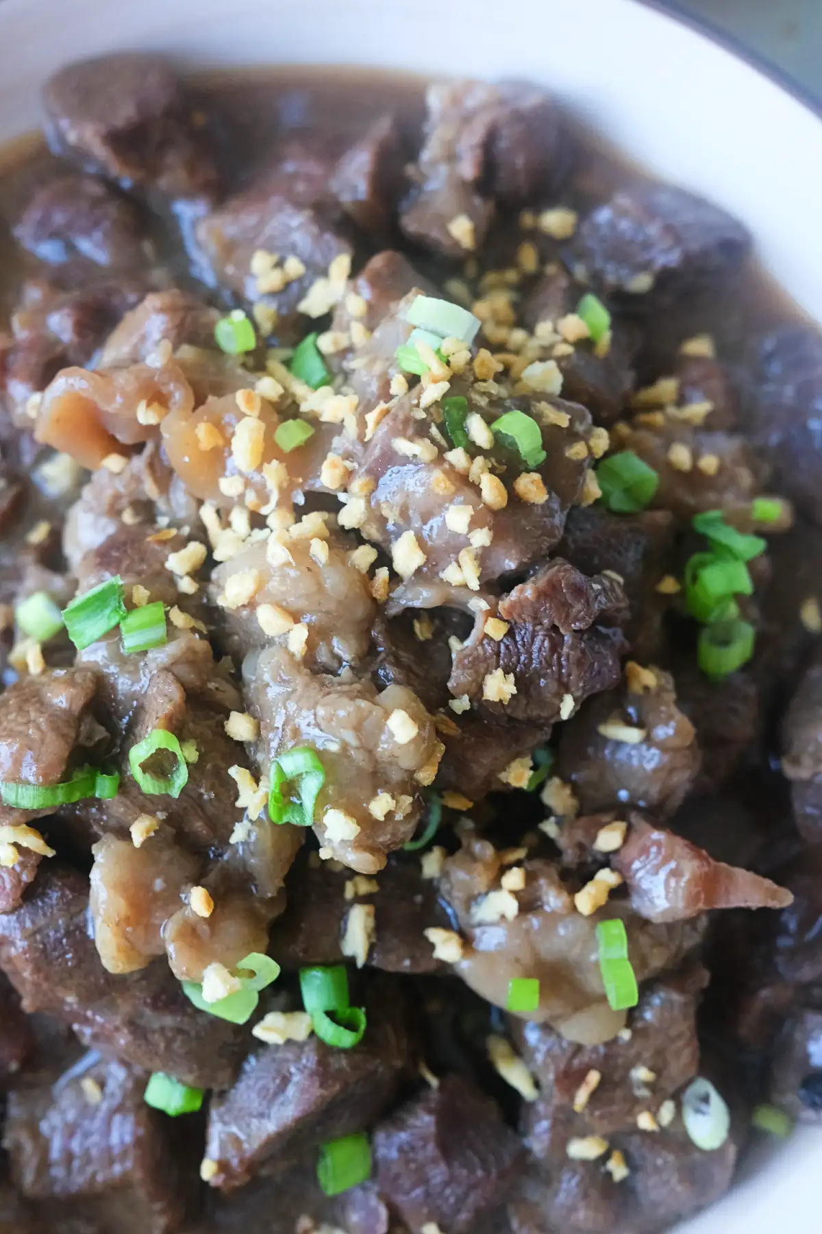 Close-up of tender beef pares in a thick sweet and savory sauce, topped with fried garlic and green onions.