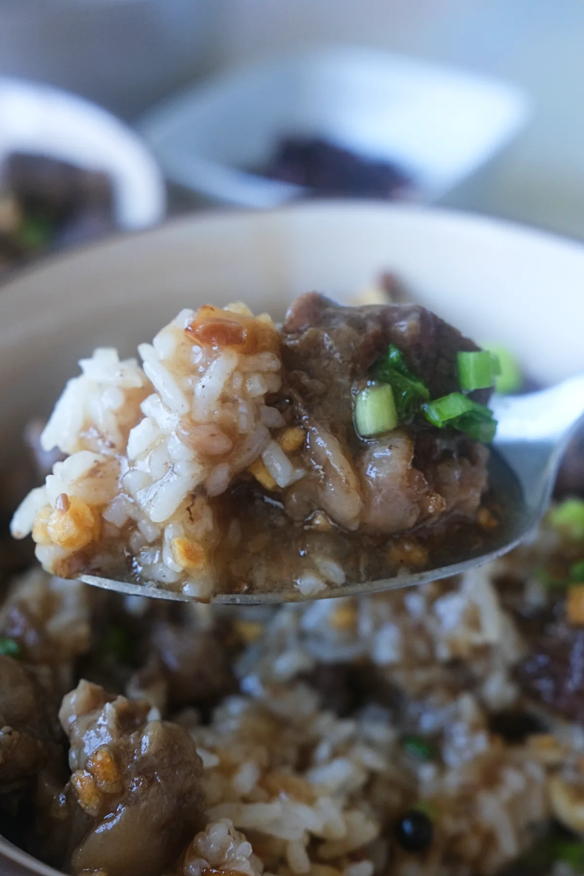 Spoon lifting tender pieces of Filipino beef pares topped with fried garlic and green onions.