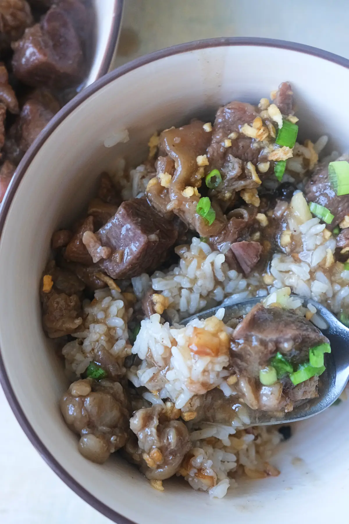 Bowl of Filipino beef pares served over garlic fried rice with fried garlic and green onions.