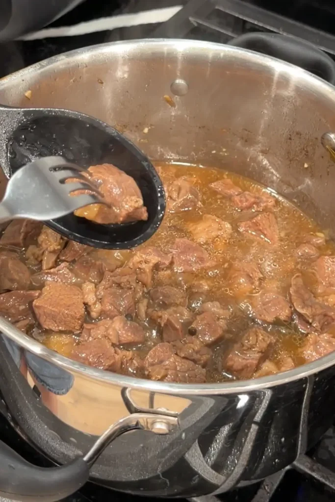 A piece of simmered beef being checked for tenderness with a fork.