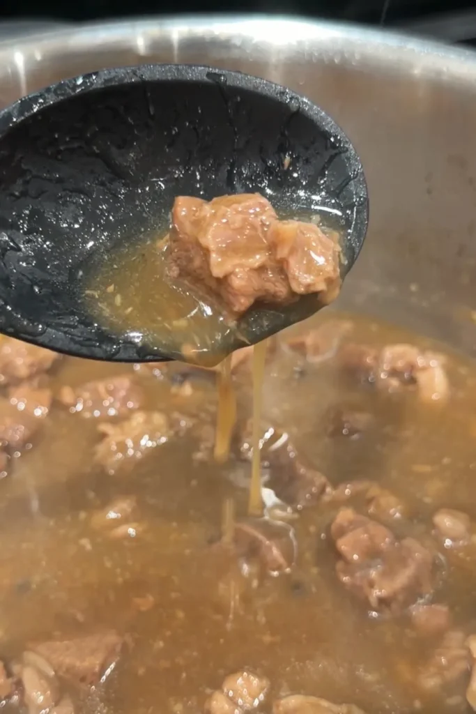 Beef pares simmering in a thickened brown sauce with ginger and aromatics.