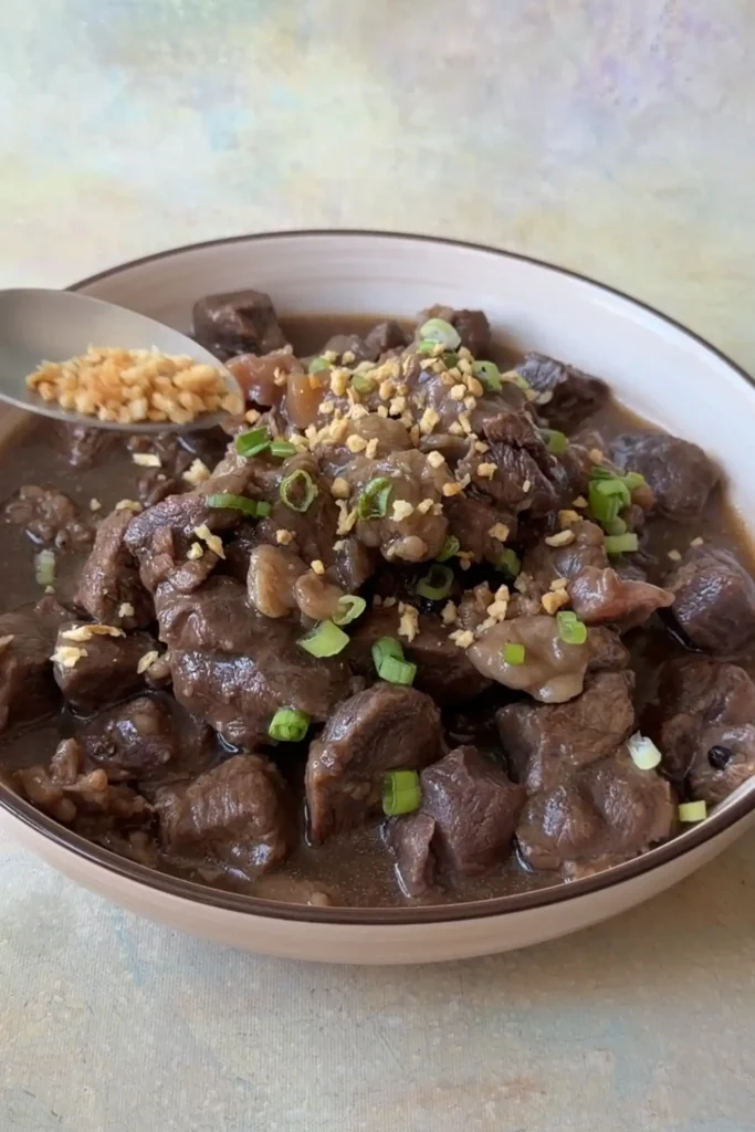 Homemade Filipino beef pares garnished with chopped green onions and crispy garlic.