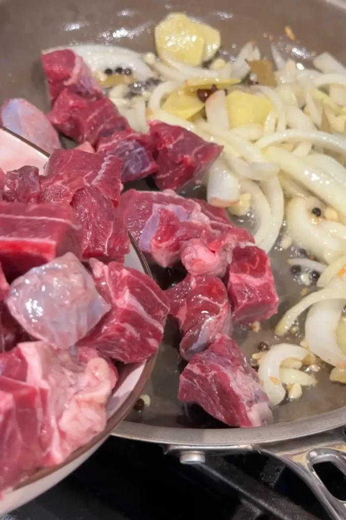 Cubed beef being added to the sautéed aromatics and spices for Filipino beef pares.
