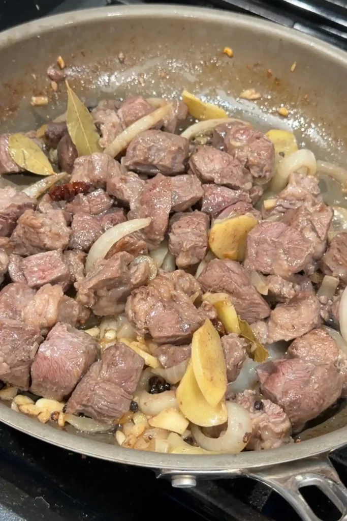 Beef cubes browning with onions, garlic, ginger, bay leaves, star anise, and peppercorns.
