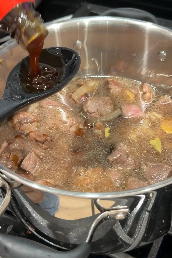 Oyster sauce being measured over the pot of beef pares.