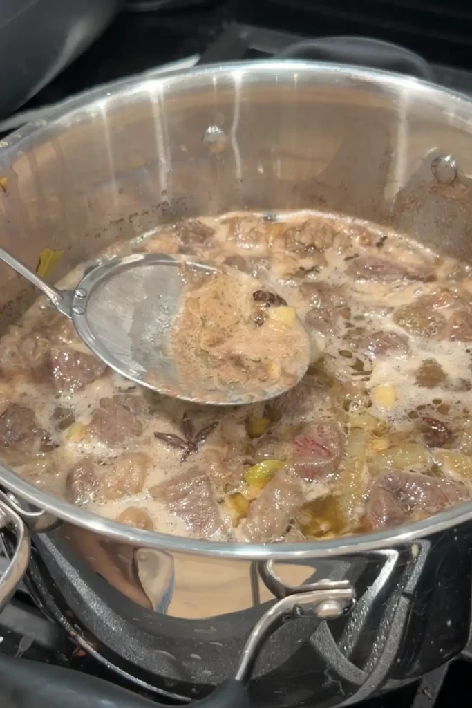 Foam being skimmed from the surface of simmering beef pares.