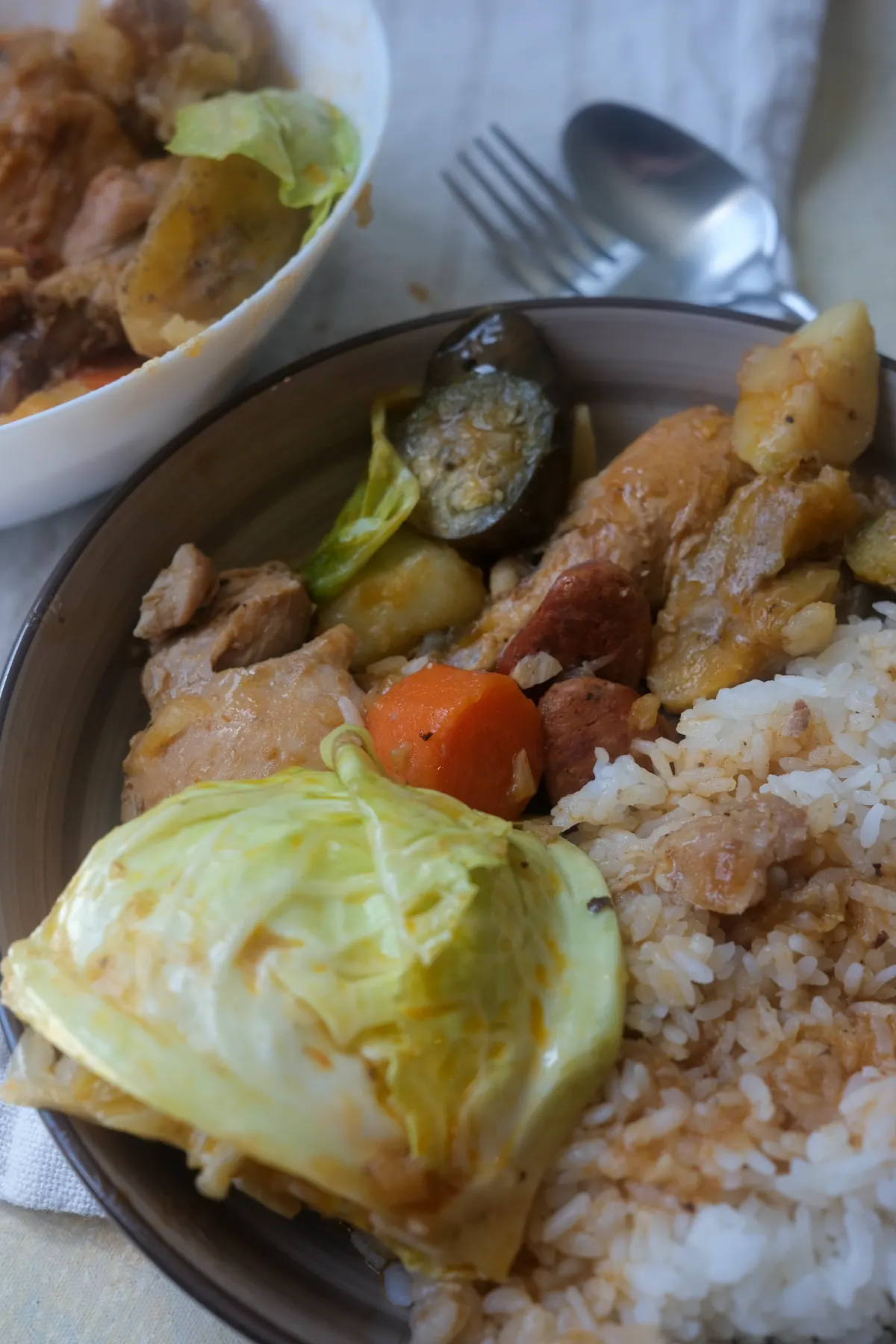 Plate of chicken pochero with rice, chorizo, saba bananas, carrots, eggplant, and cabbage