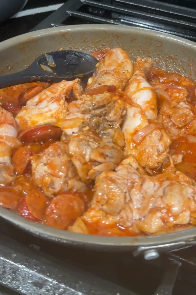 Browned chicken and Chorizo de Bilbao cooking in tomato sauce for chicken pochero