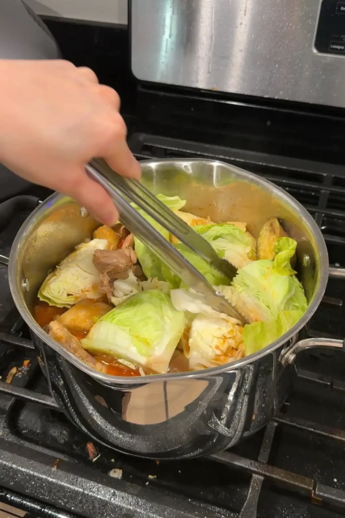 Cabbage being added to a pot of chicken pochero