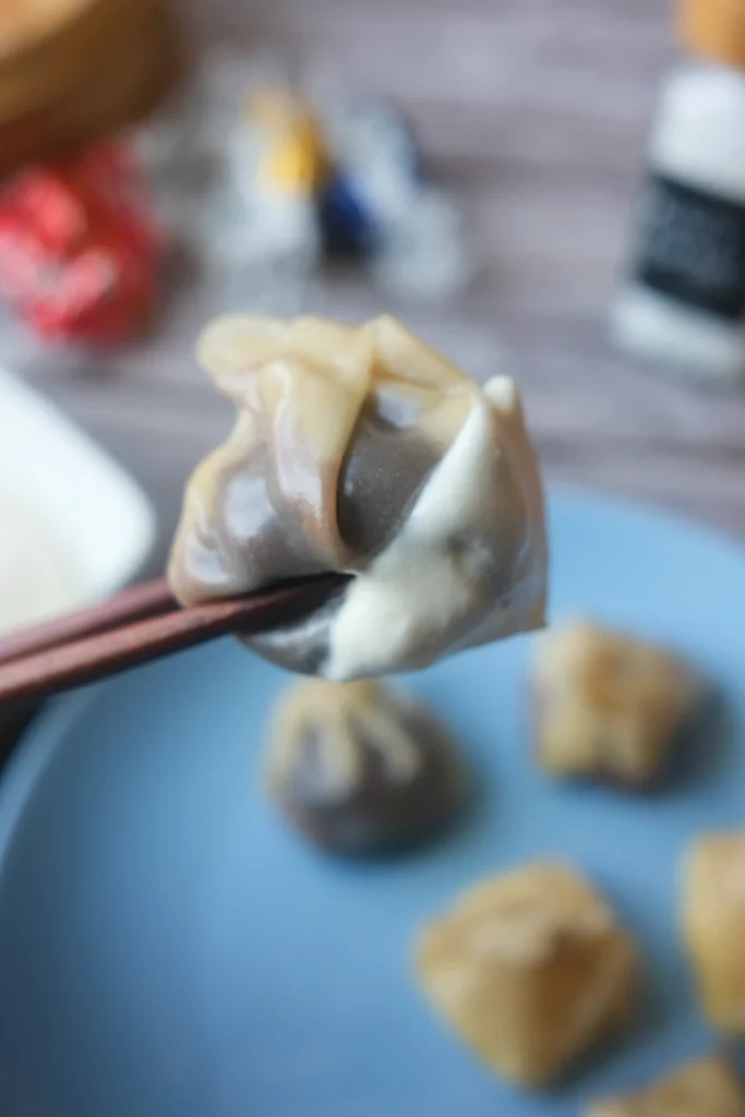 Steamed chocolate dumpling held with chopsticks, served with fluffy salted caramel cream on a blue plate.