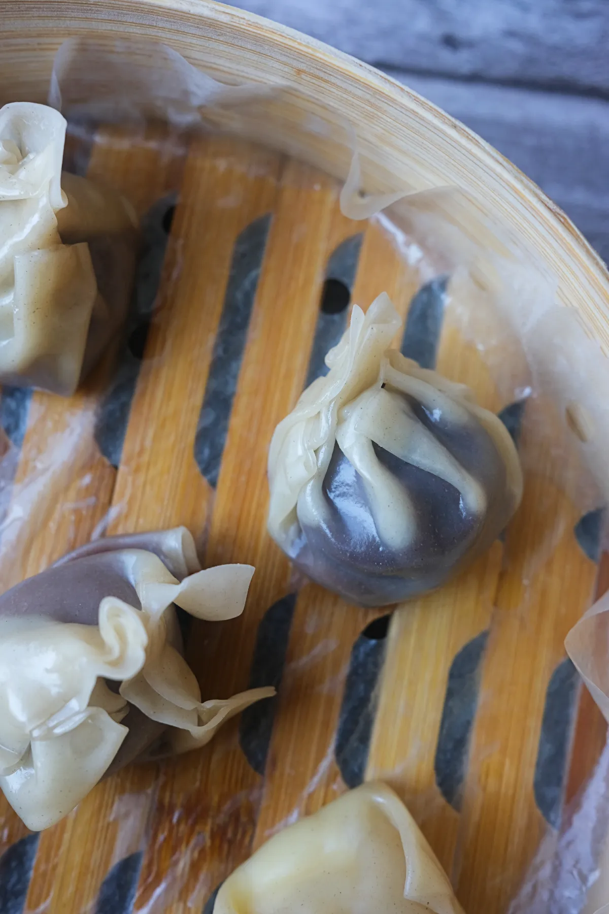 Close-up of steamed chocolate dumplings with soft, translucent wonton wrappers in a bamboo steamer.