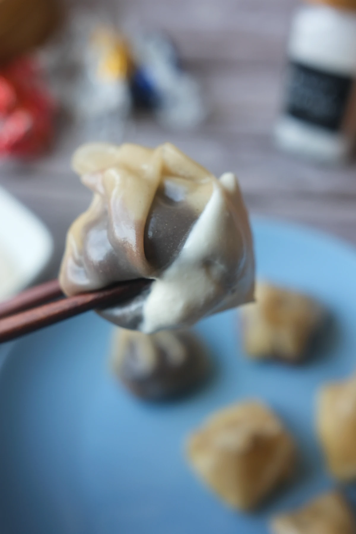 Steamed chocolate dumpling held with chopsticks, served with fluffy salted caramel cream on a blue plate.