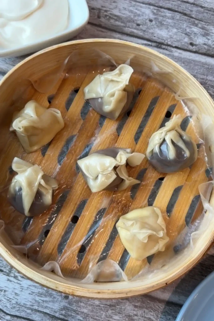 Freshly steamed chocolate dumplings resting in a parchment-lined bamboo steamer, ready to serve with salted caramel cream.