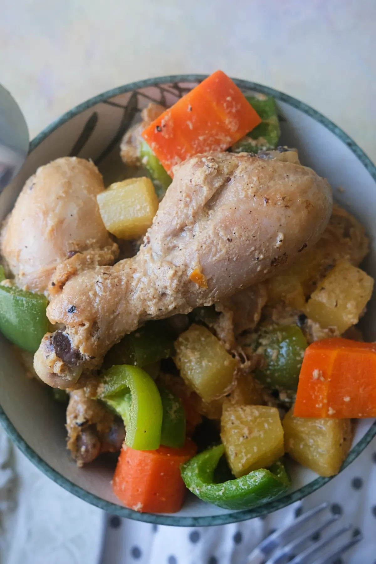 Filipino Pininyahang Manok with chicken drumsticks, pineapple chunks, carrots, and green bell peppers in a creamy sauce.