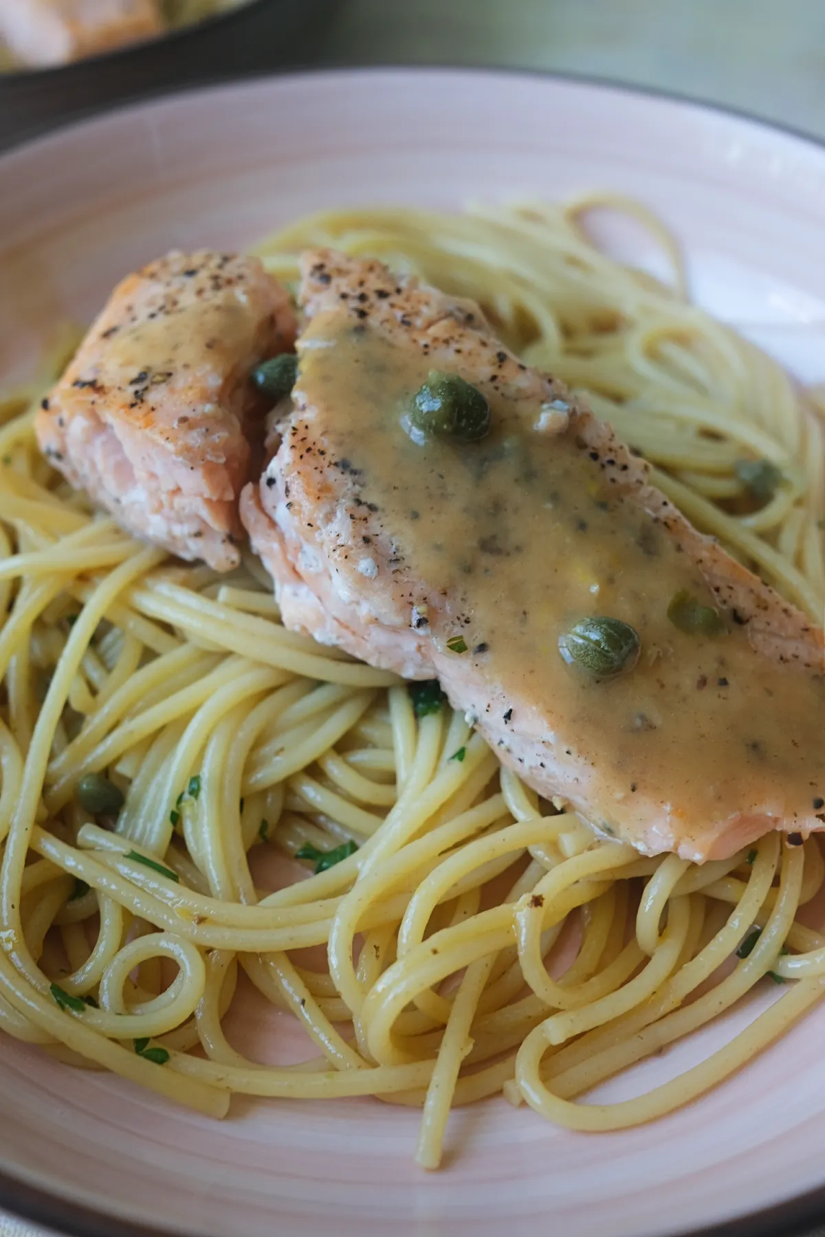 Pan-seared salmon fillet with lemon caper sauce served over spaghetti.