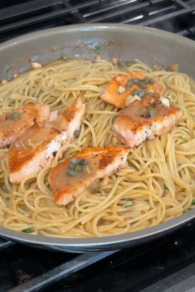 Pan-seared salmon arranged over spaghetti with lemon caper sauce.