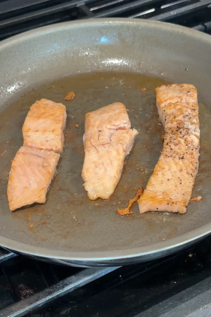 Pan-seared salmon fillets cooking until lightly golden.