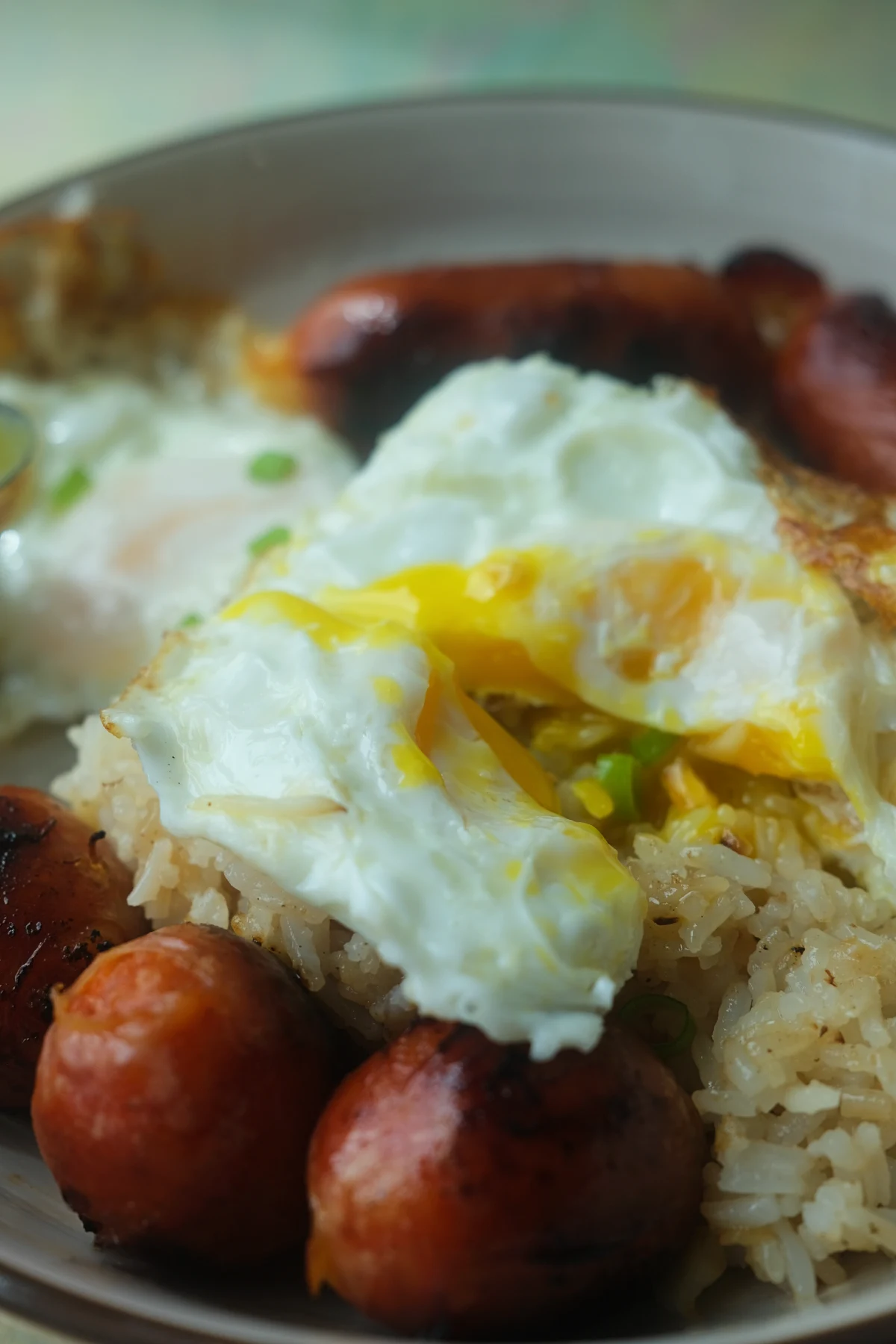 Runny fried egg yolk over garlic fried rice and longganisa in a Filipino silog meal