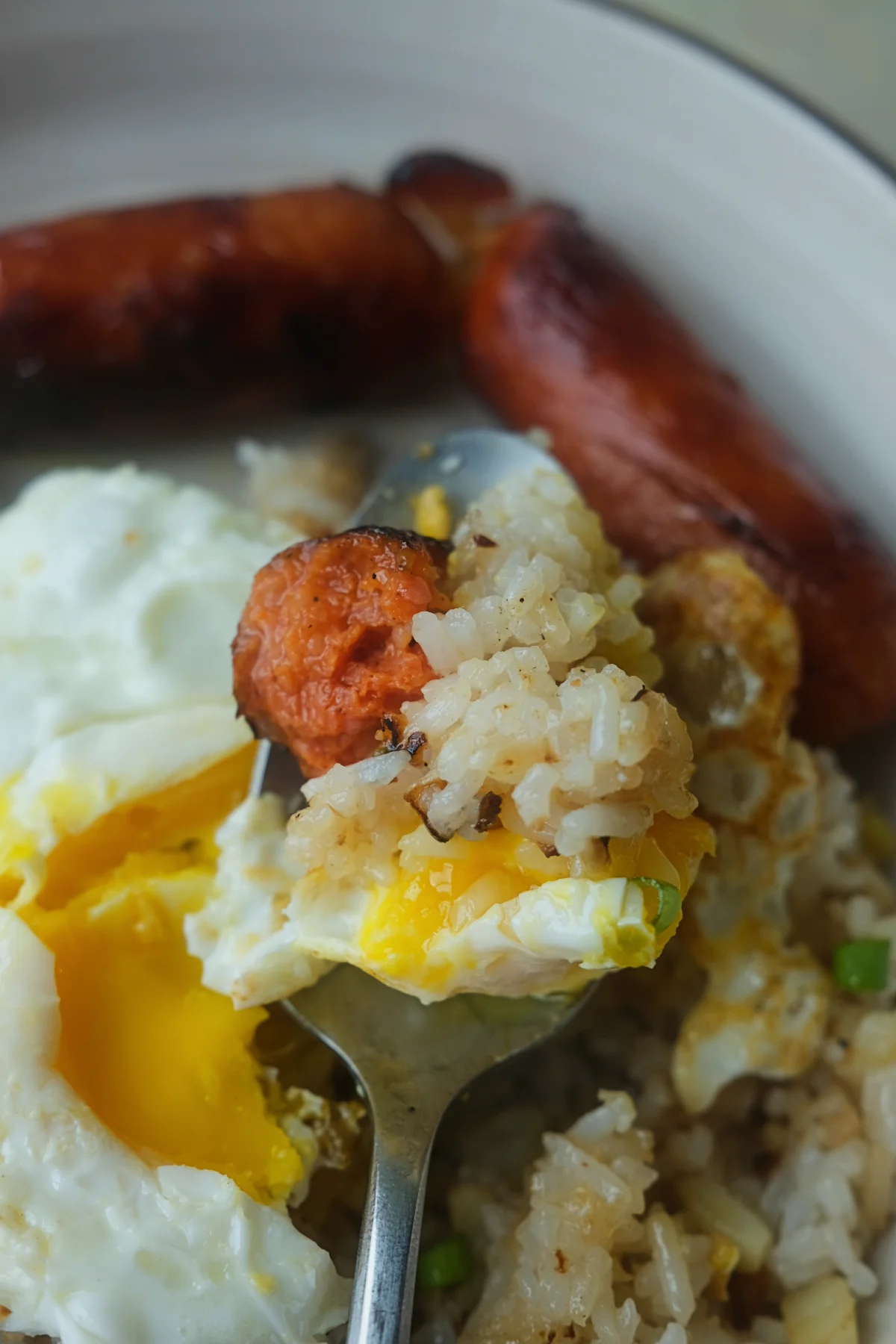 Bite of longganisa, garlic fried rice, and runny fried egg from a longsilog breakfast