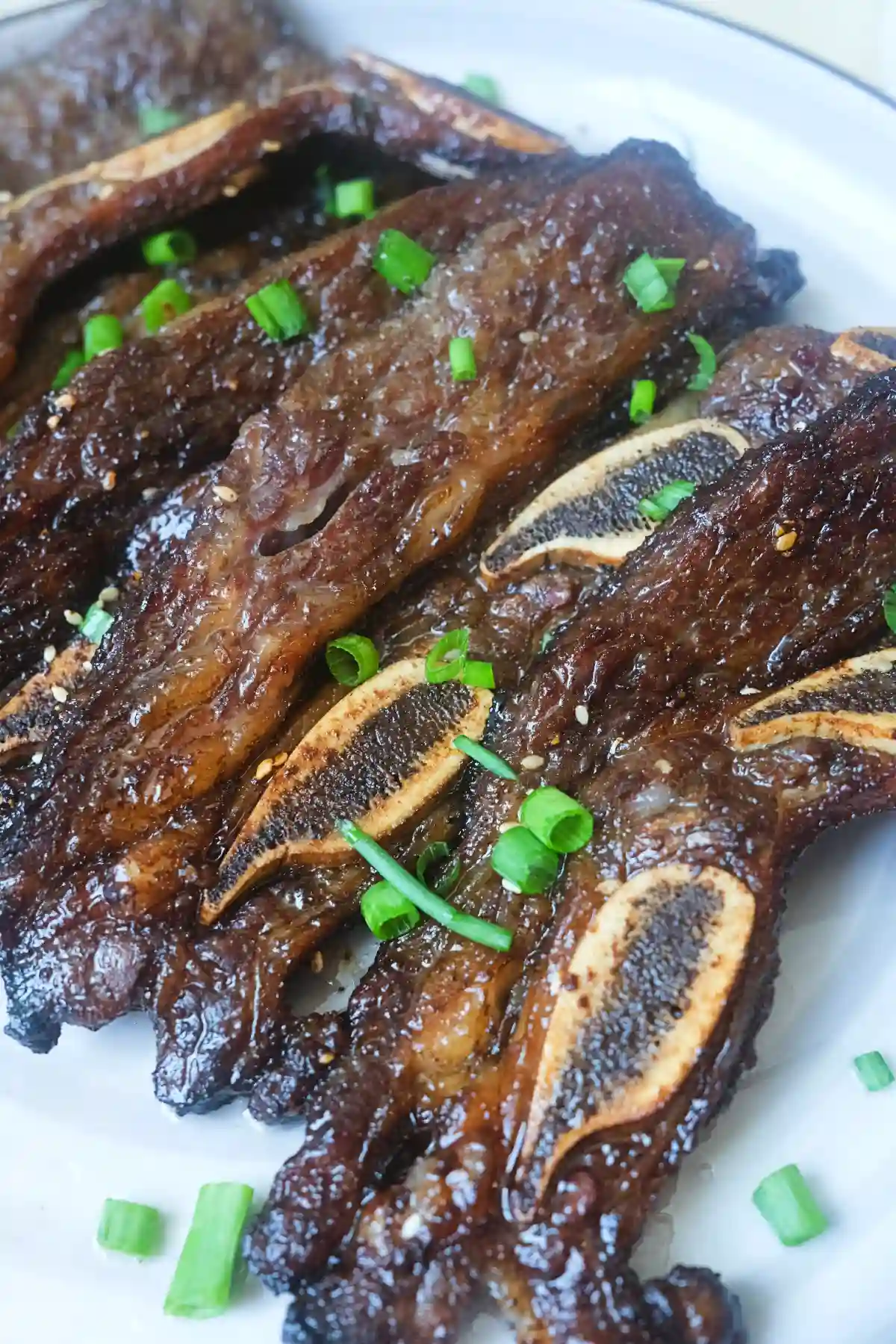 Air fryer Korean short ribs garnished with chopped green onions and sesame seeds on a white plate.