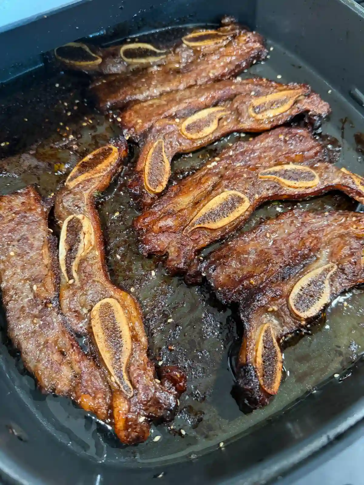 : Thin-cut Korean beef short ribs cooking in an air fryer basket until browned and caramelized.