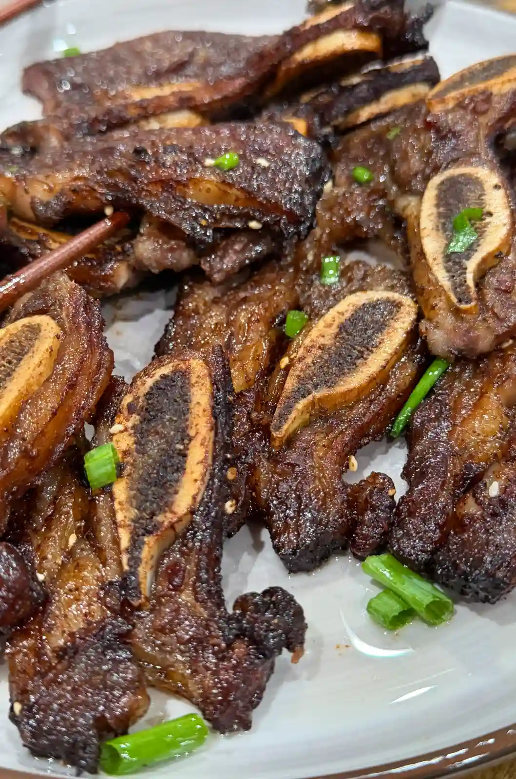 Cooked beef short ribs in the air fryer basket with browned edges and exposed cross-cut bones.